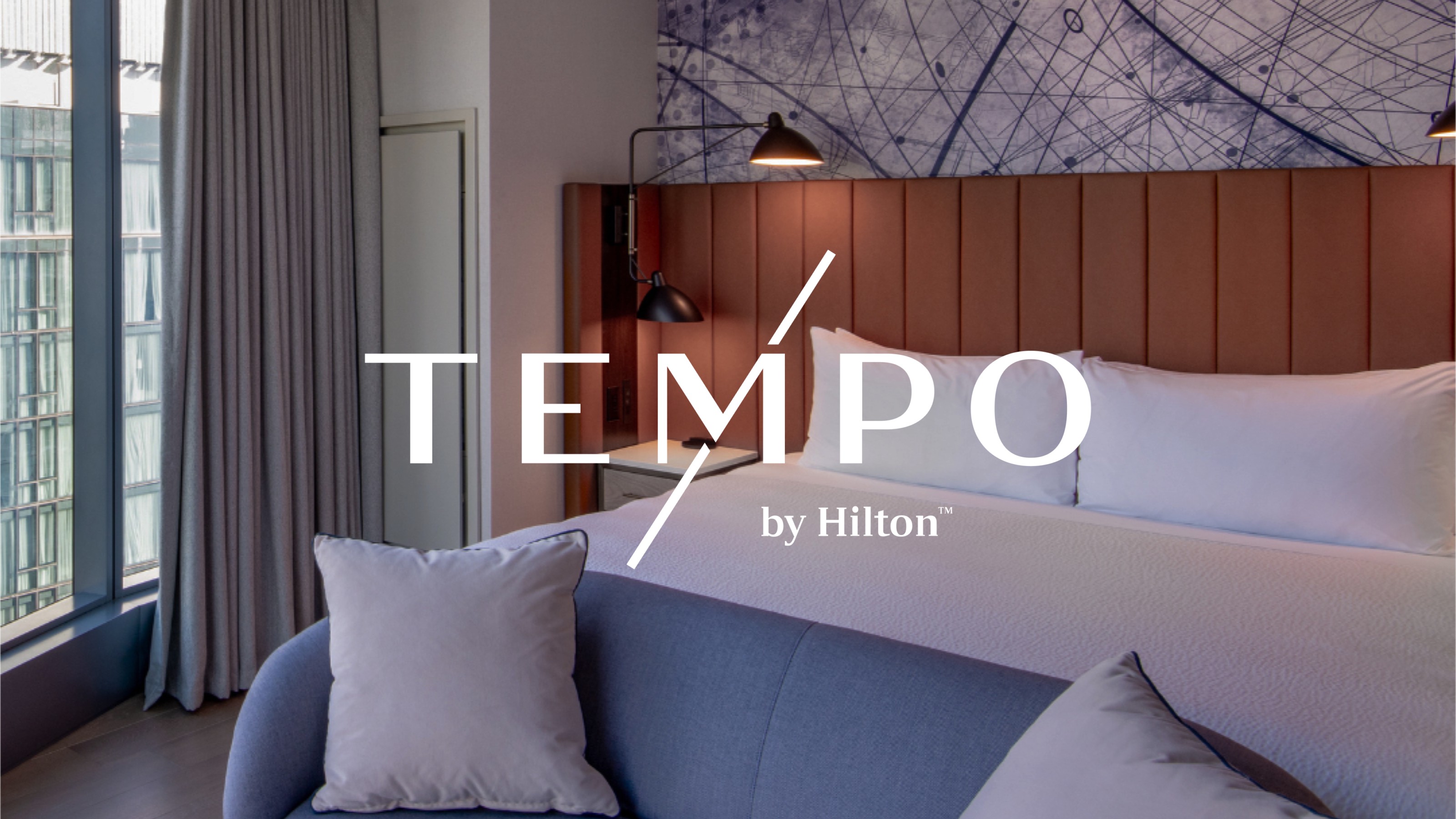 A﻿n image of a Tempo hotel room focusing on bedding with the Tempo logo by Hilton overlayed over the photograph.